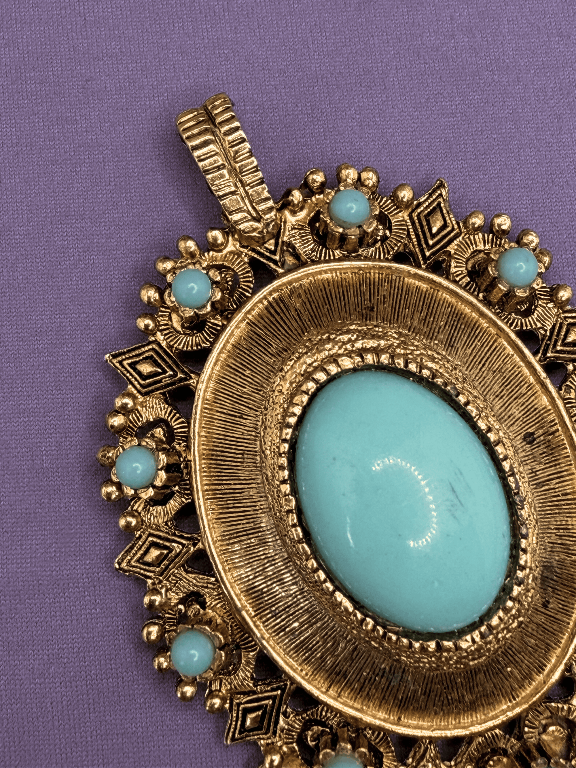 Decorative pendant with gold frame and turquoise stones on a purple background