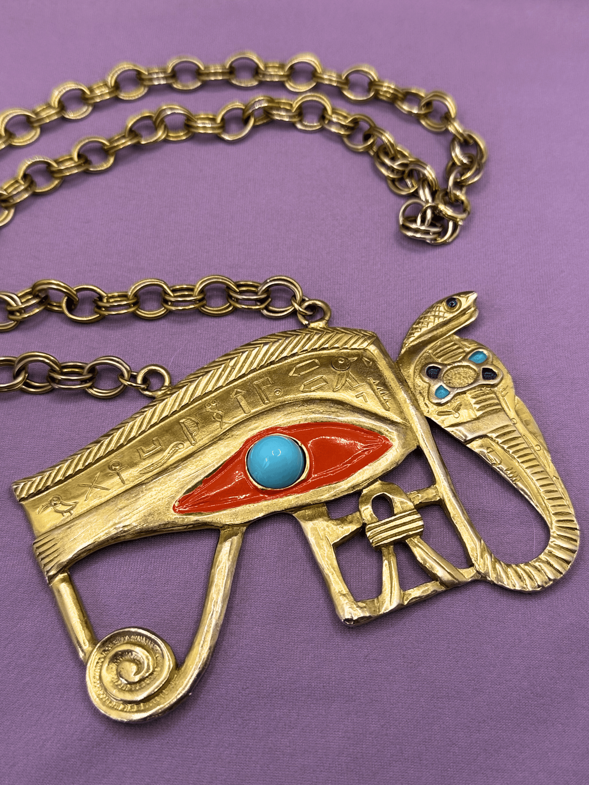 Gold necklace with an eye of Horus pendant on a purple background